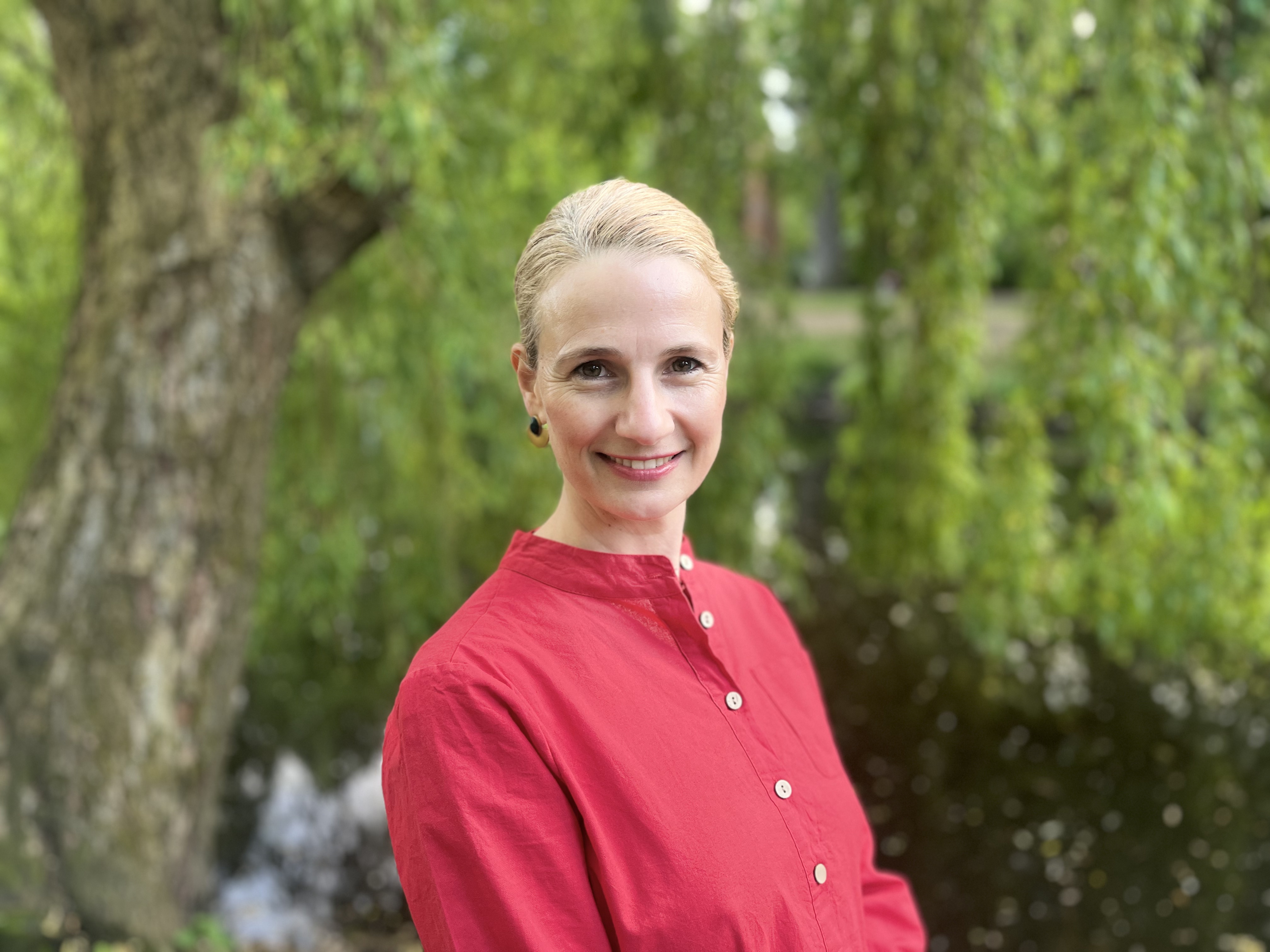 Natalie Wollenschneider steht in rotem Shirt vor einer Trauerweide