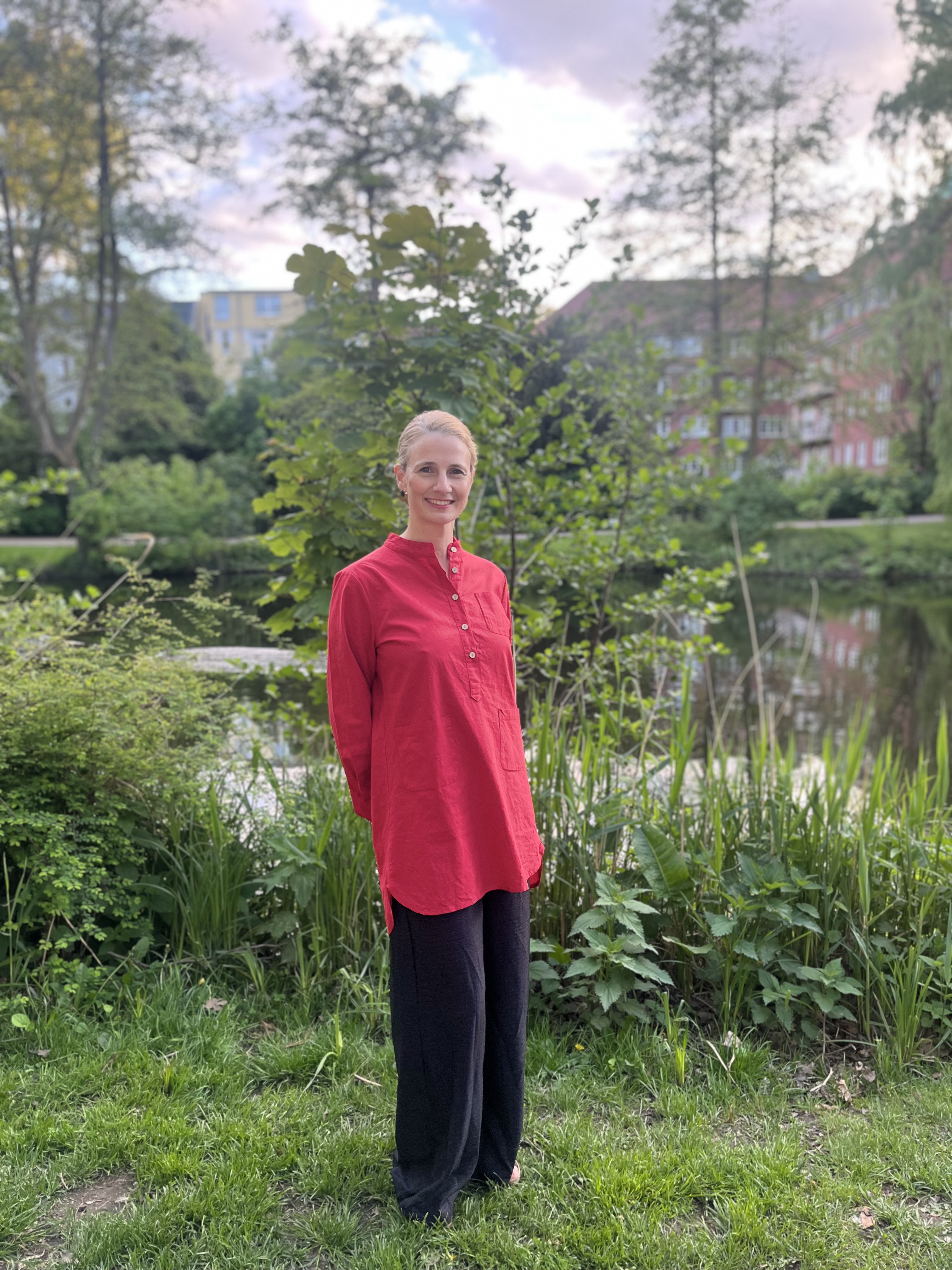 Natalie Wollenschneider steht im roten Shirt an einem Teich, umgeben von üppigem Grün