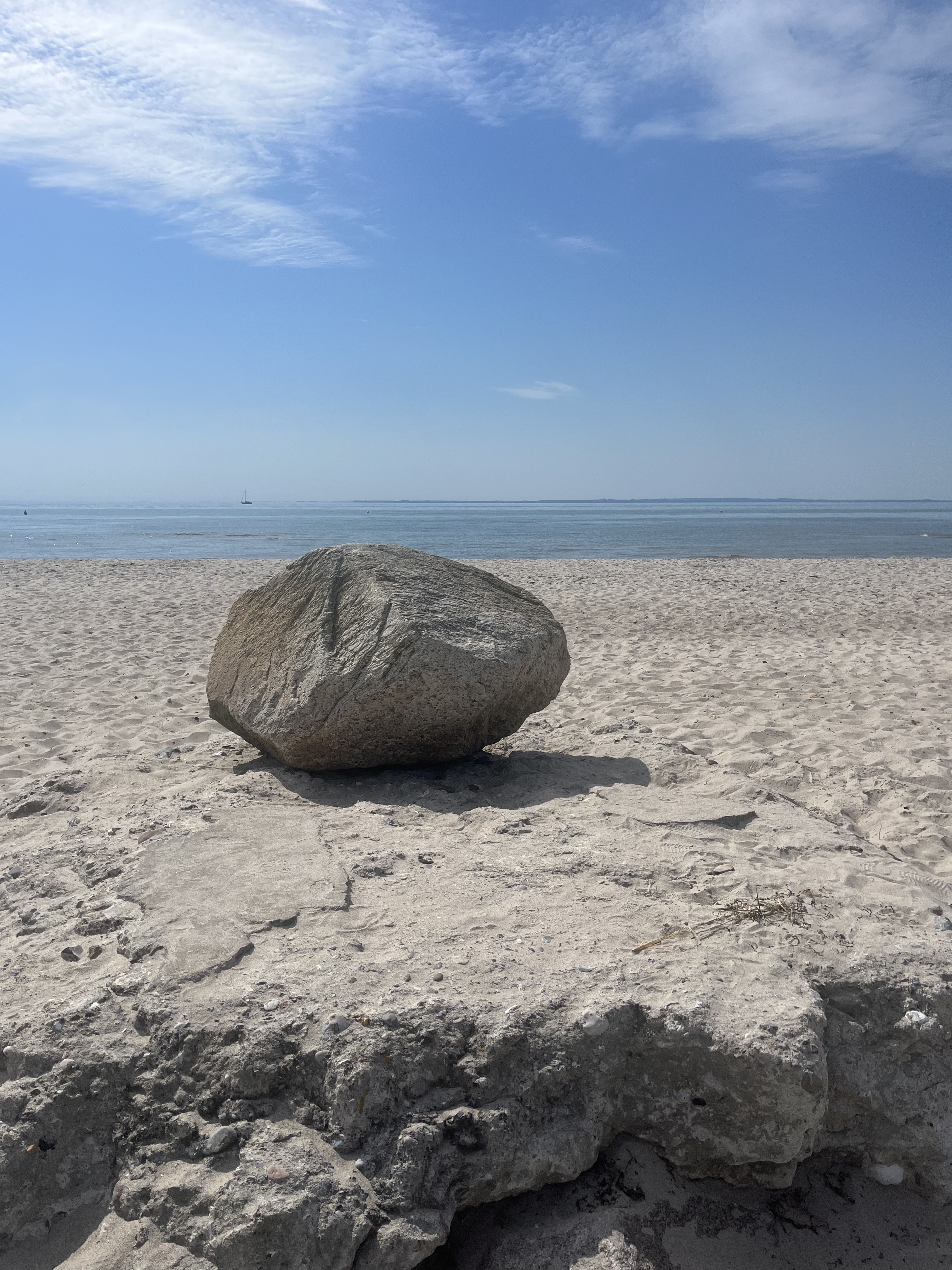 Großer Stein an einem sandigen Strand mit ruhiger See und blauem Himmel